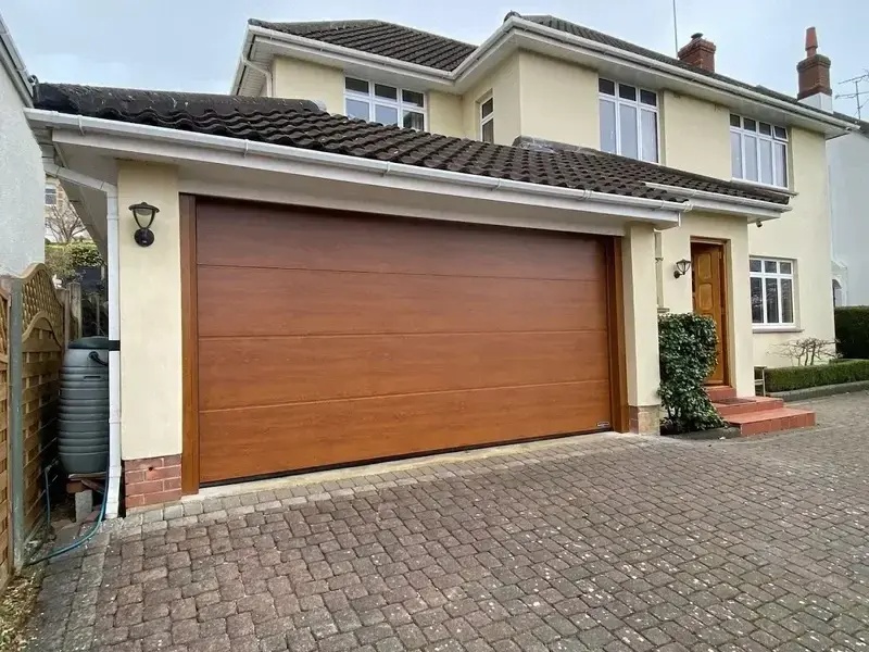 Wide golden oak sectional garage door installed on detached family home with block paved driveway