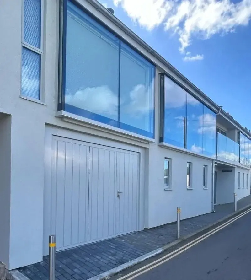 White vertical-panel garage door on contemporary white rendered building with large glass balcony above spring failure fix